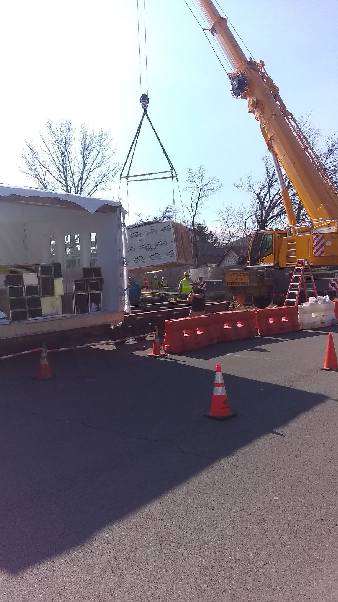 Low-angle view of crane boom beside brick building with sun flare