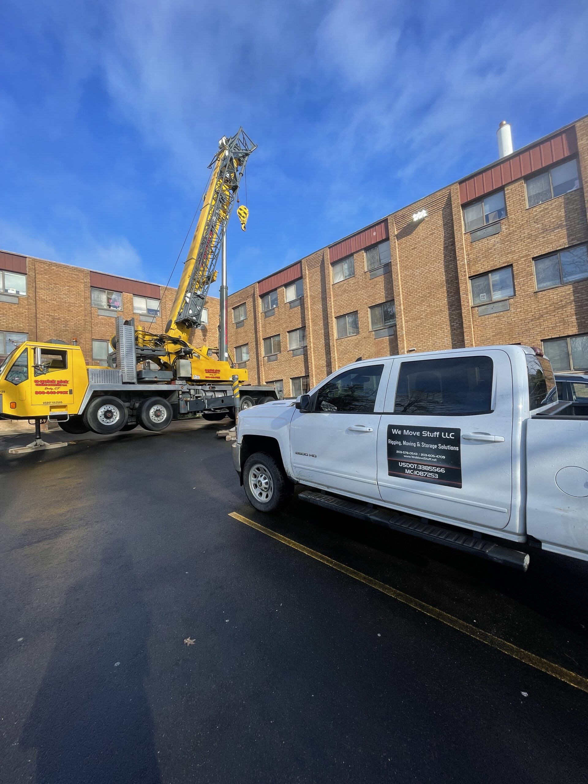 Crane lifting modular building wall panel section with workers below guiding placement