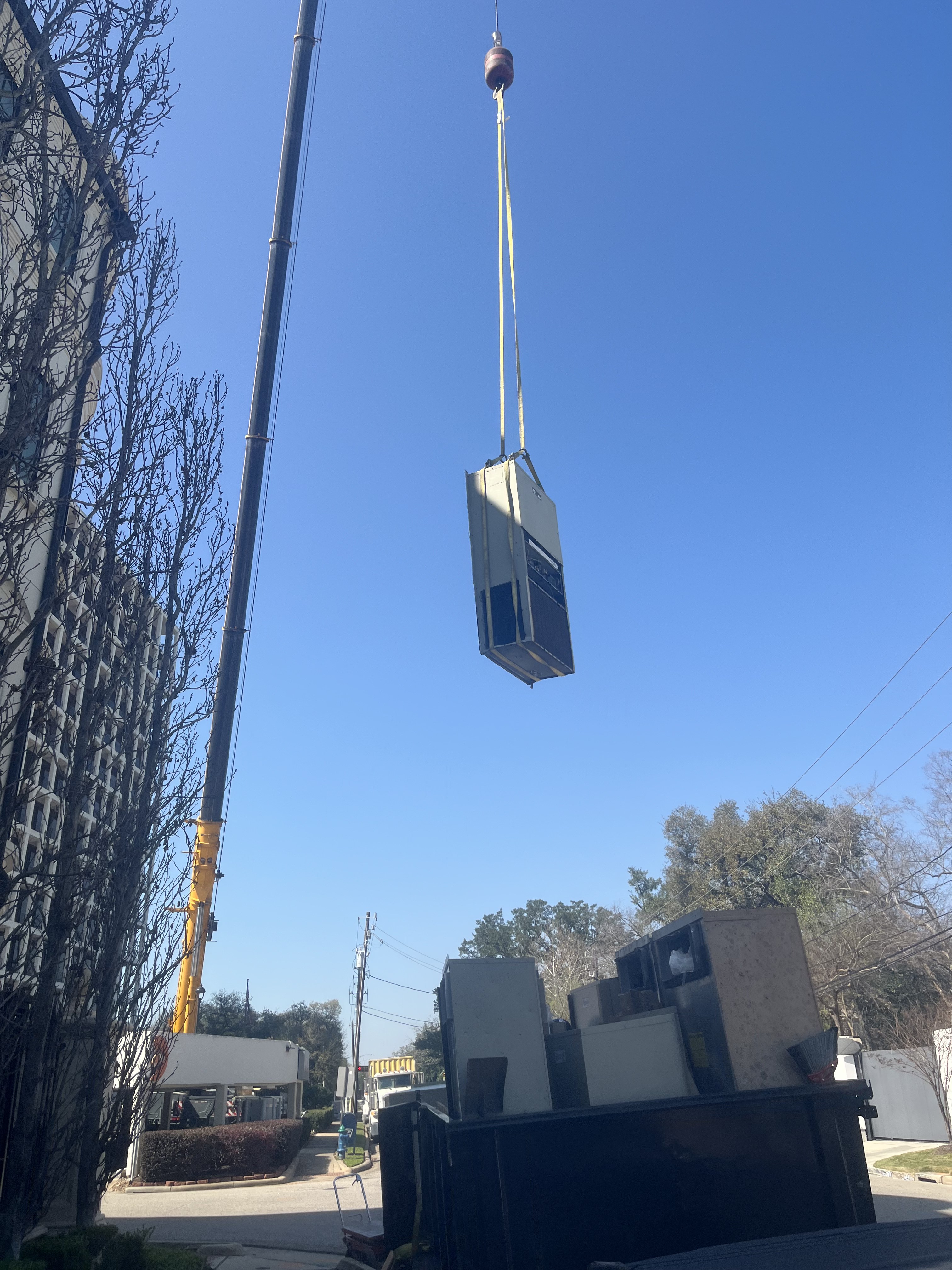 HVAC air handler being hoisted with old equipment in dumpster below