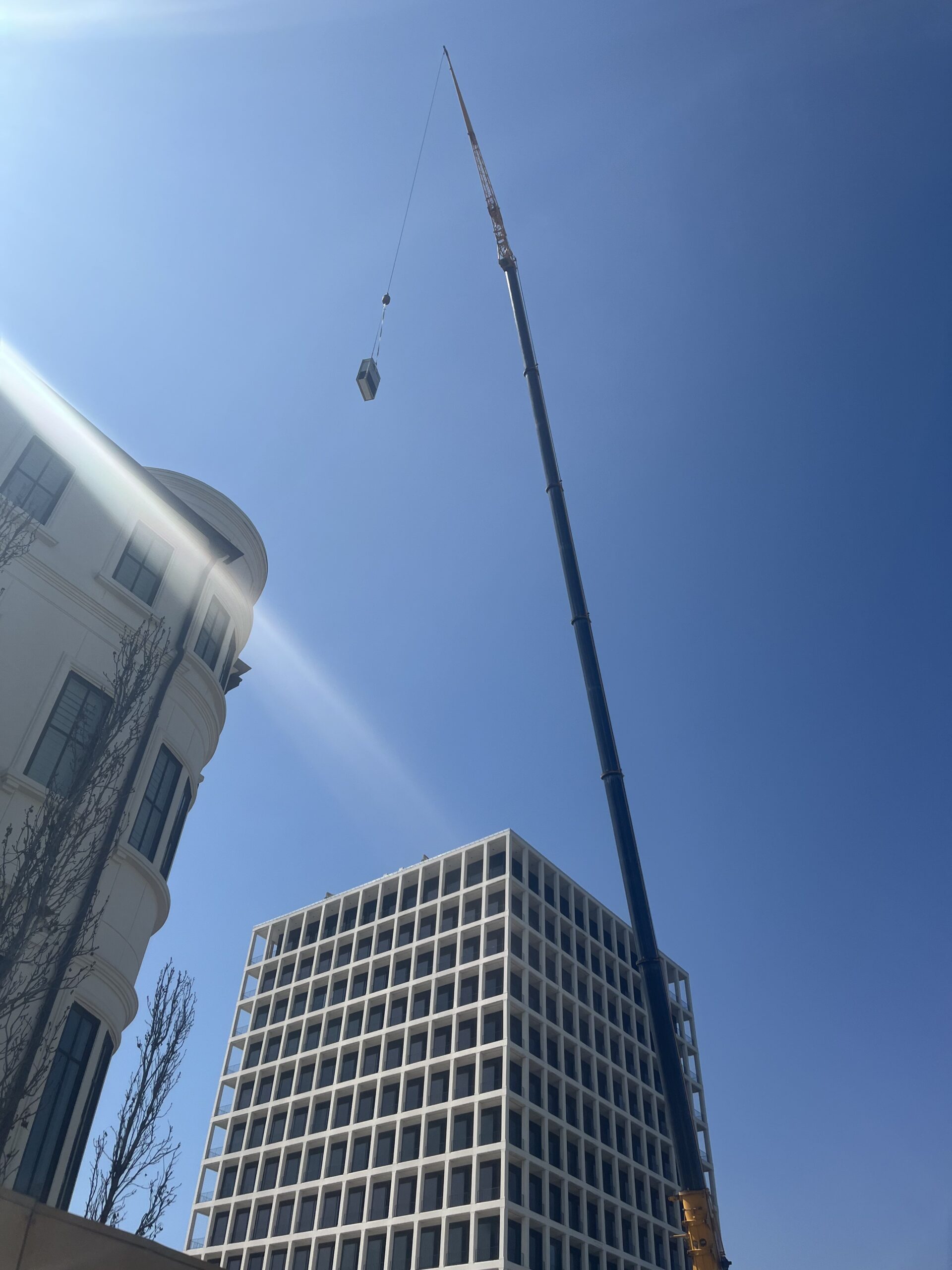 Wide shot of crane at San Felipe street corner beside white grid tower building