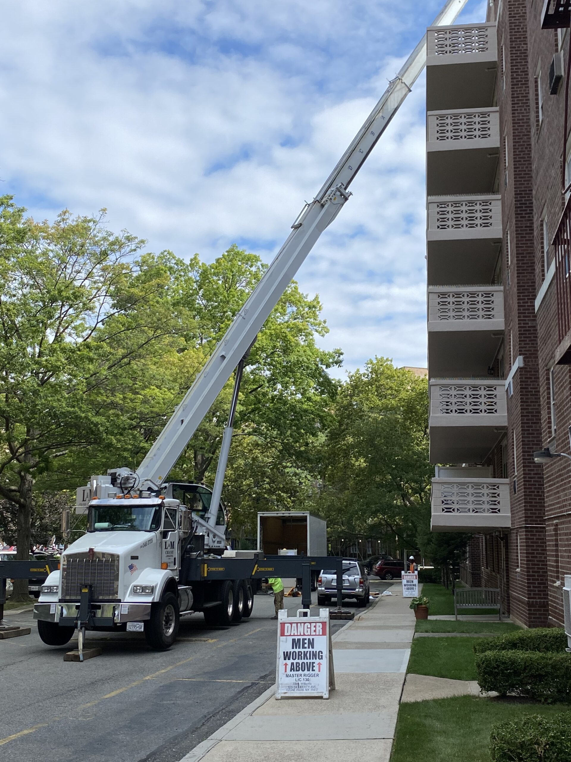 L&M Crane truck beside brick apartment building with Danger Men Working Above sign