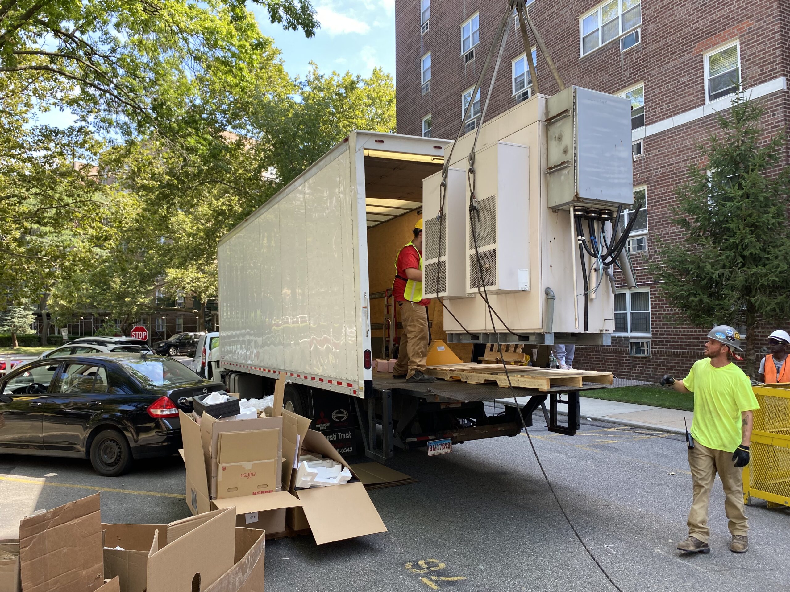 Workers loading large HVAC unit onto box truck with liftgate